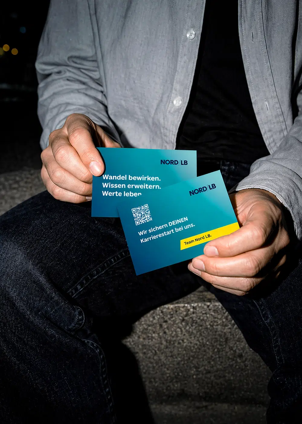 Eine Person hält zwei türkisblaue NORD/LB-Visitenkarten zum Karrierestart mit QR-Code in den Händen.