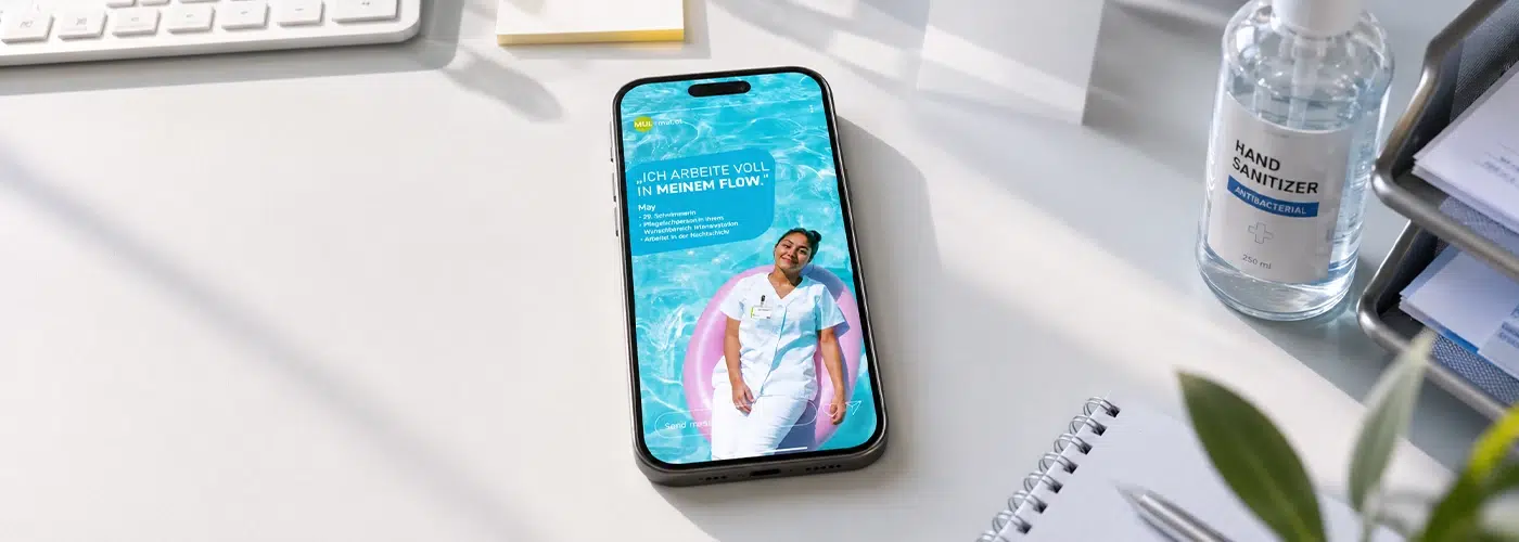 Smartphone auf einem Schreibtisch zeigt eine Anzeige mit einer Pflegekraft in einem Pool und dem Slogan Ich arbeite voll in meinem Flow.