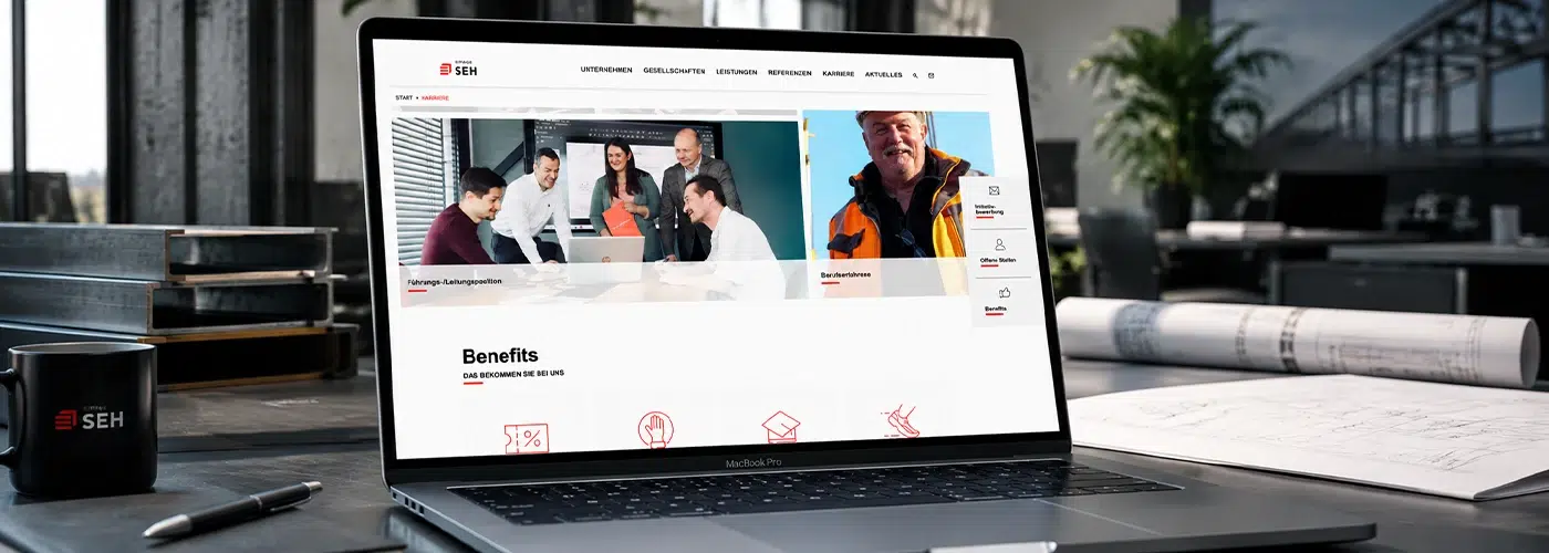 Laptop mit der Karriereseite von SEH Engineering auf einem Schreibtisch mit Bauplänen und Stahlträgern.