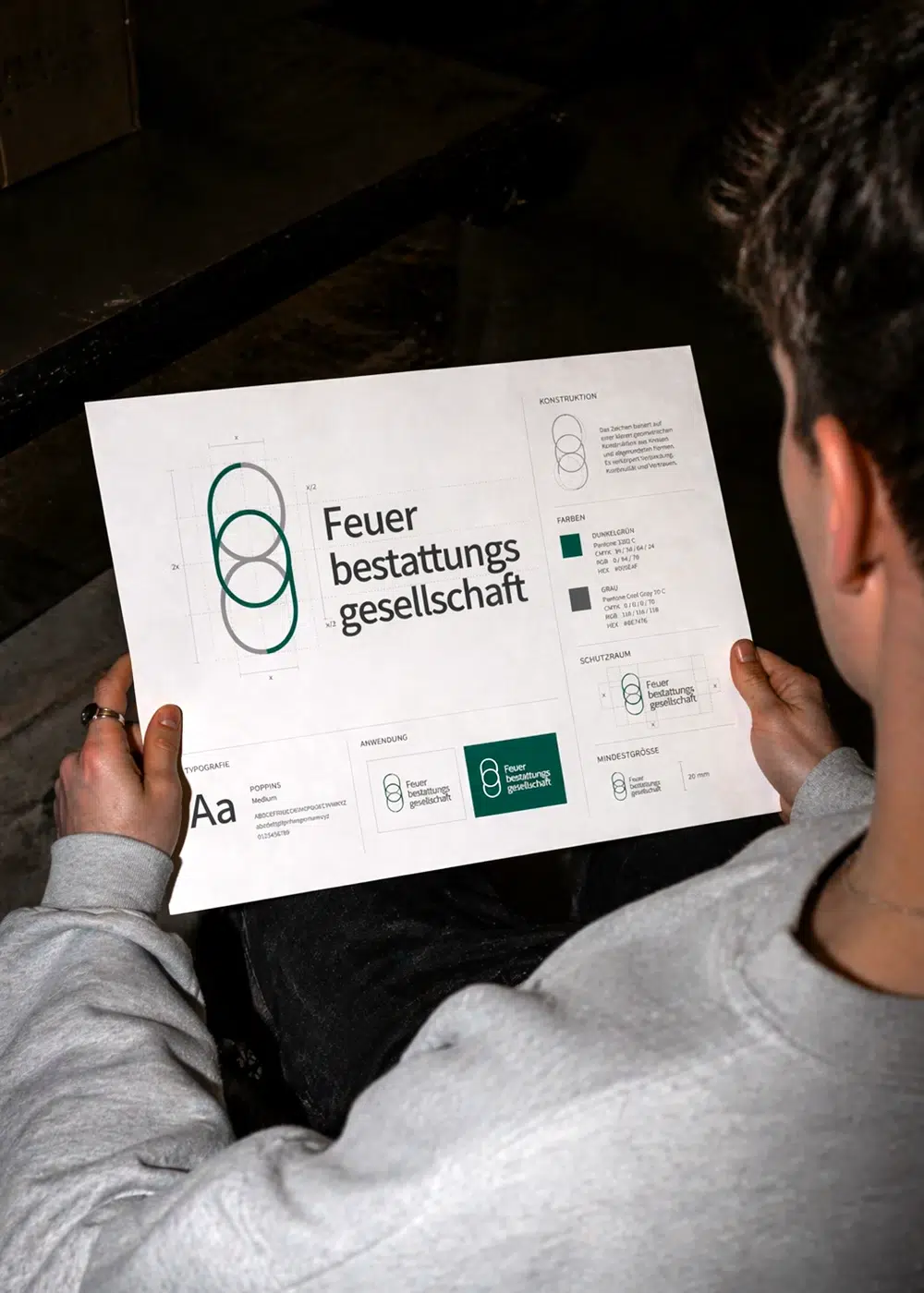 Eine Person hält ein Blatt Papier mit der Logo-Herleitung und dem Corporate Design der Feuerbestattungsgesellschaft.