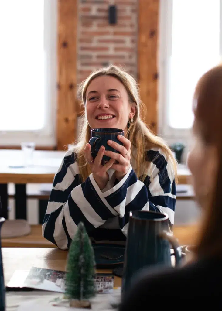 Eine lächelnde junge Frau im gestreiften Pullover hält eine Tasse beim klartxt Hackathon.
