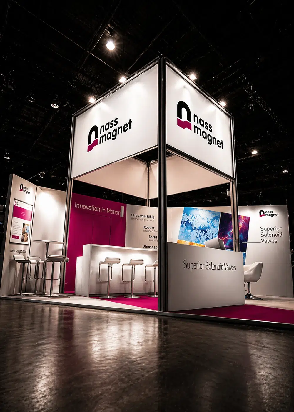 Moderner Messestand der Firma nass magnet mit Informationstresen, Barhockern und beleuchtetem Markenlogo.