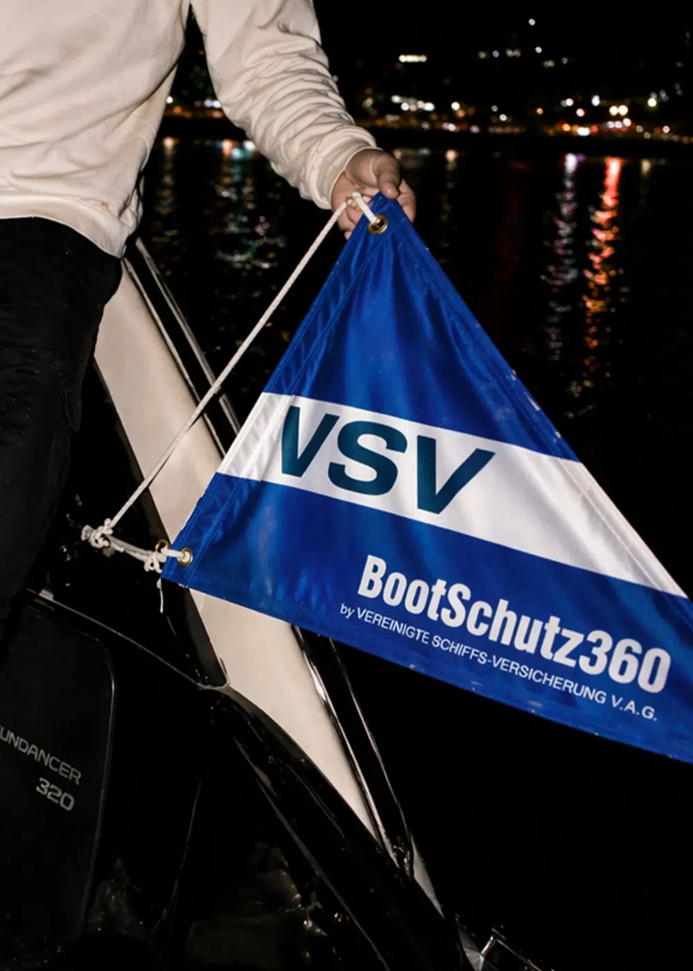 Person hält eine VSV BootSchutz360 Flagge an Bord eines Bootes bei Nacht.