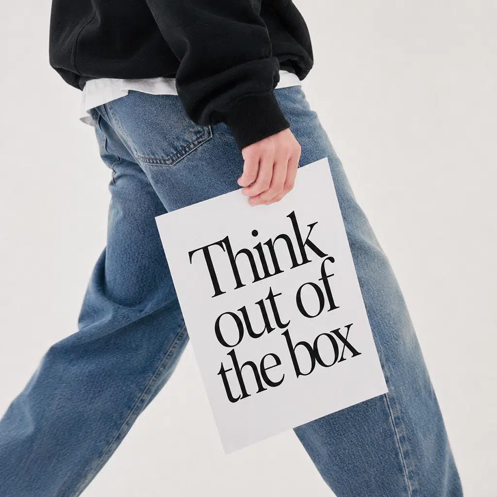 Eine Person in Jeans trägt ein Schild mit der Aufschrift Think out of the box.